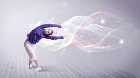 A beautiful young hip hop dancer dancing contemporary urban street dance in front of grey wall background with smokey lines and glitter concept.