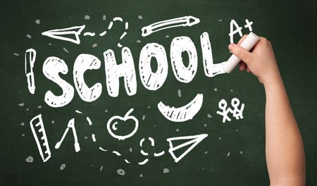 A teacher writing school, drawing children things on clean green chalkboard by hand