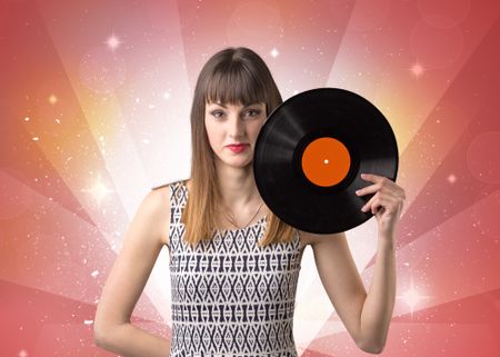 Young lady holding vinyl record on a red background with lights shining behind her