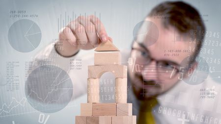 Young handsome businessman using wooden building blocks with data and numbers around him