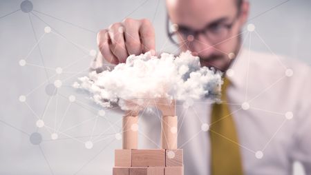 Young handsome businessman using wooden building blocks behind cloud concept 