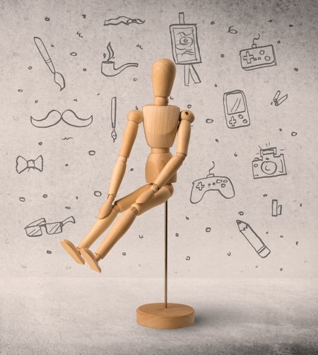 Wooden mannequin posed in front of a greyish background with hobby related scribbles behind it