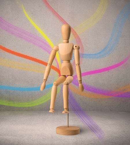 Wooden mannequin posed in front of a greyish background with colorful lines behind it