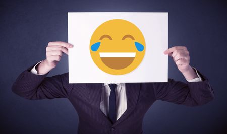 Young businessman hiding behind a laughing emoticon on cardboard