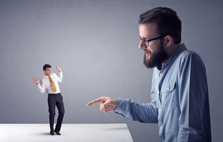 Young professional businessman being angry with an other miniature businessman in front of a grey background