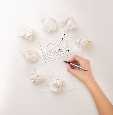 Female hand next to a few crumpled paper balls drawing a progress chart