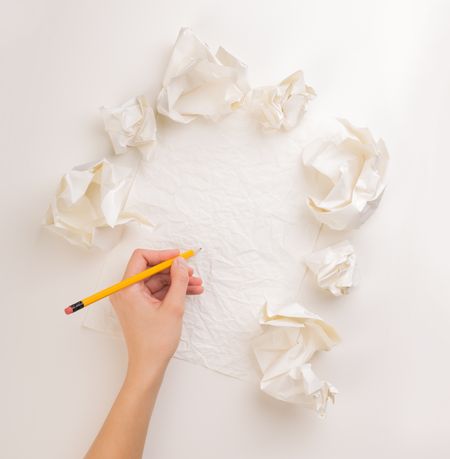 Female hand trying to write next to a few crumpled paper balls 