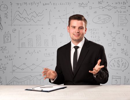 Young handsome businessman sitting at a desk with white charts behind him