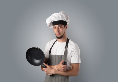 Young bearded cook portrait with kitchen tools and empty wallpaper 
