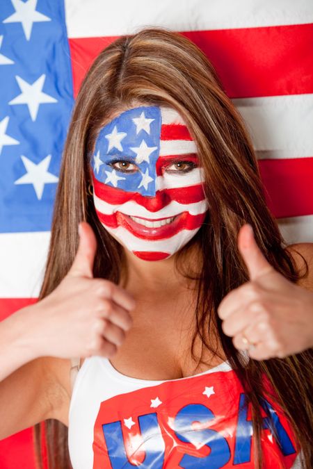 Happy American woman with the USA flag painted on her face with thumbs up