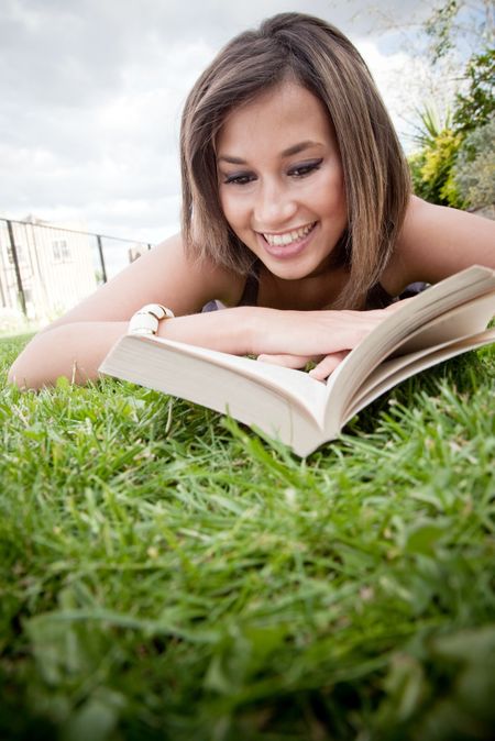 Woman lying on the floor outdoors and reading a book