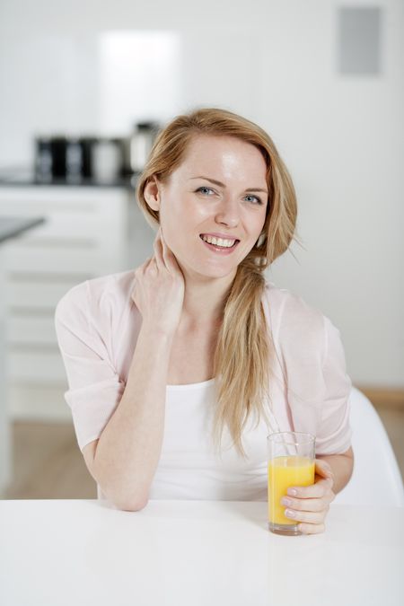 Young woman in pink shirt sitting at dining table at home with orange juice