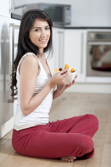 Young woman enjoying a bowl of fresh fruit in her kitchen