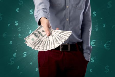 Young businessman holding large amount of bills with green background and currency symbols 