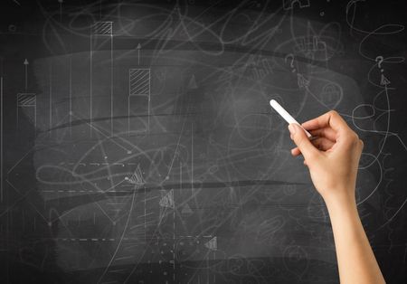 Female hand holding white chalk in front of a blackboard with scribbles and plans drawn on it