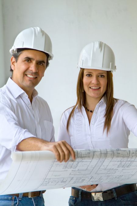 Architects at a construction site holding at blueprints and smiling