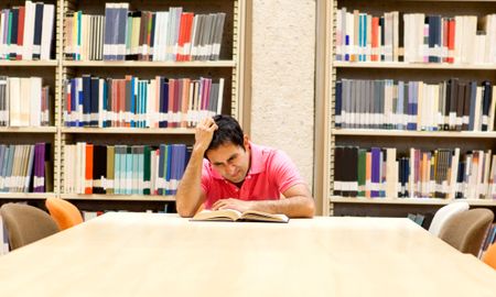 Frustrated male student reading a book at the library