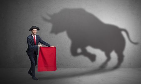 Businessman standing with red cloth in his hand and big bull shadow on the wall