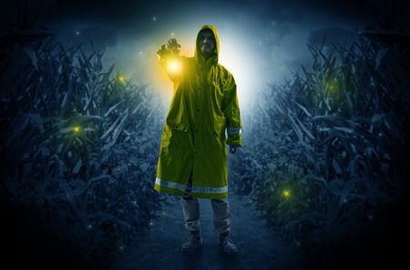 Man in raincoat at night coming from thicket and looking something with glowing lantern