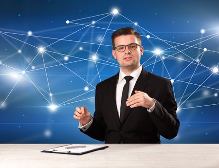 Young handsome businessman sitting at a desk with a blue connection graphic behnid him