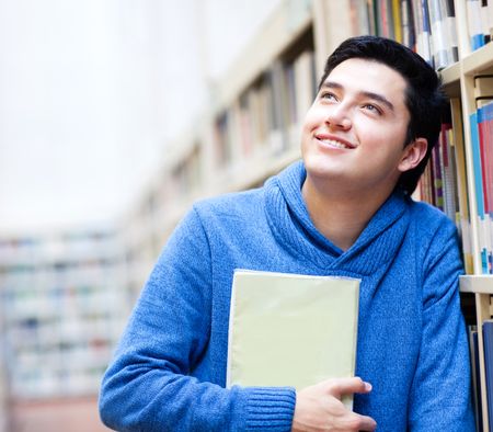 Thoughtful male student at the library holding a book