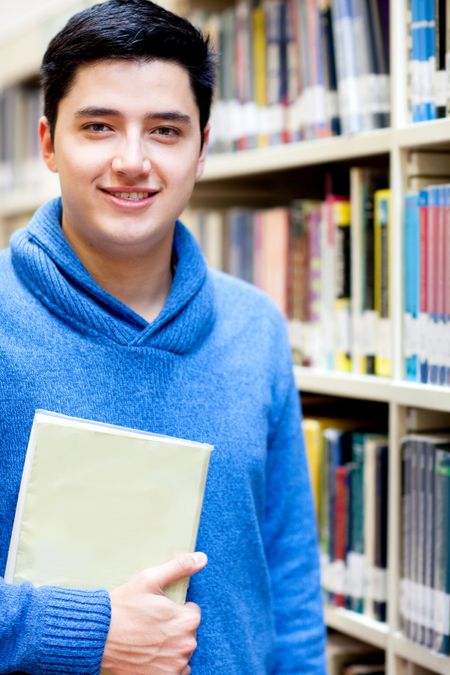 Young man at the library holding a book and smiling