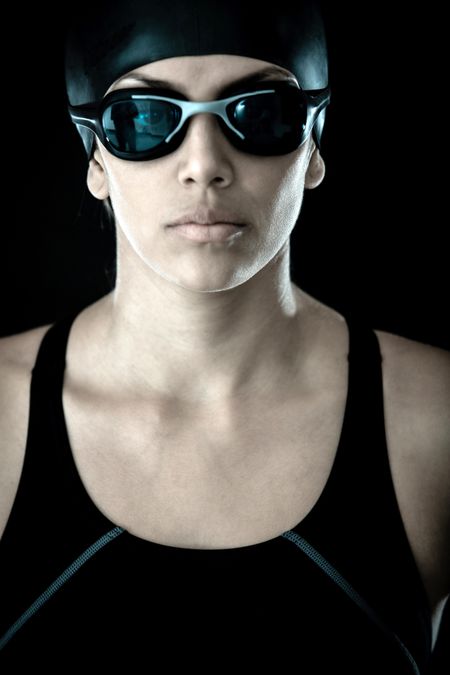 Professional female swimmer with goggles and a hat - isolated over a black background