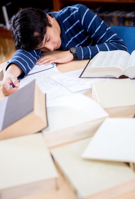 Tired student sleeping at the library while studying for a test