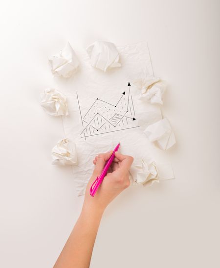 Female hand next to a few crumpled paper balls drawing a progress chart