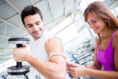 Gym man showing off muscles and woman measuring them