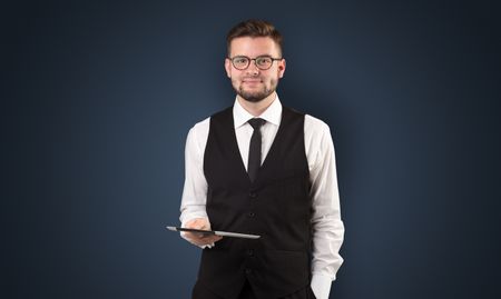 Handsome spectacled businessman holding a tablet with dark background