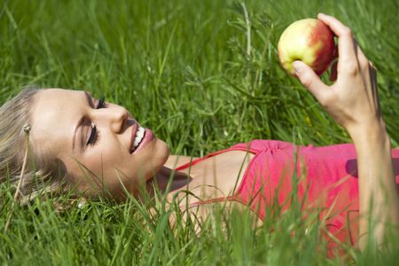 Beautiful young woman eating an apple on a summers day in the countryside.