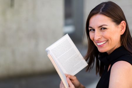 Happy woman enjoying reading a book outdoors