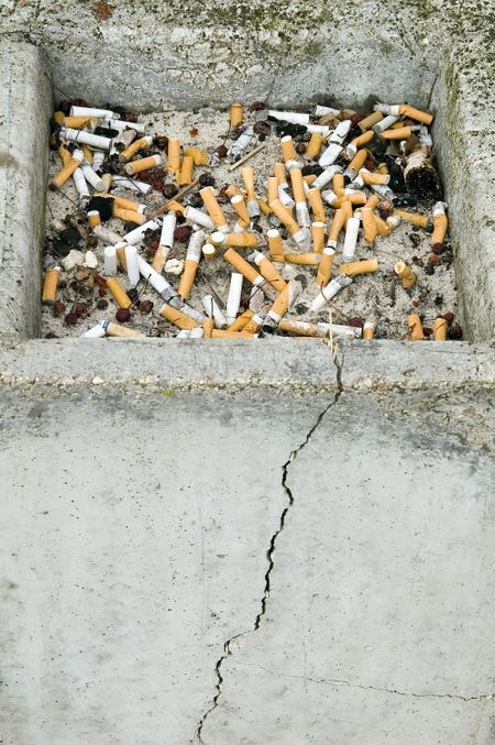 Cracked concrete ashtray full of cigarette butts