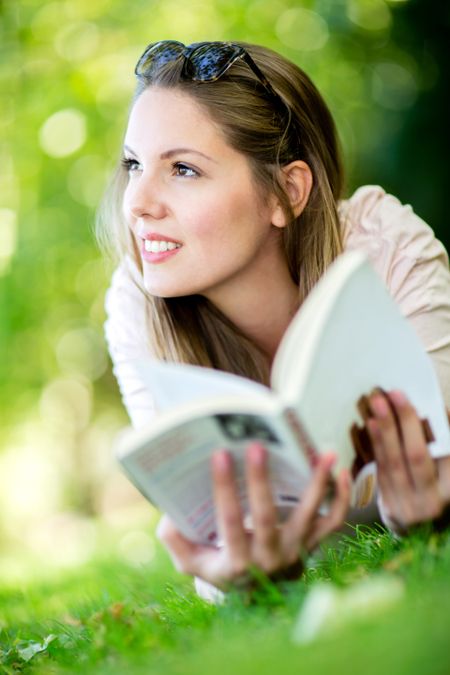 Thoughtful woman reading a book outdoors and smiling