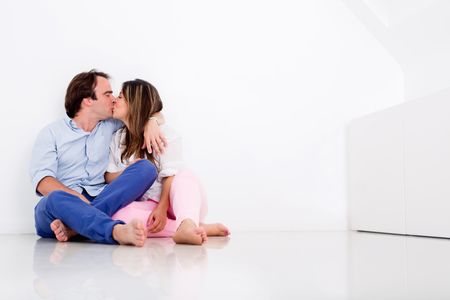 Loving couple sitting on the floor of their apartment kissing