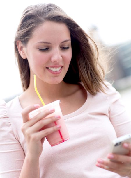 Woman enjoying a milkshake and texting on her phone