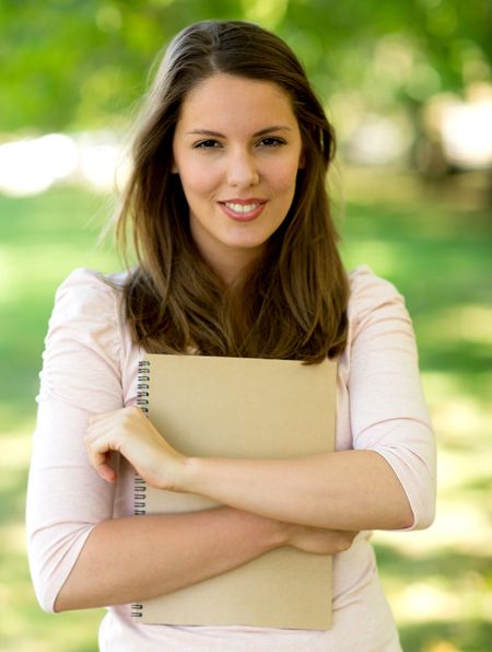 Beautiful female student outdoors holding a notebook