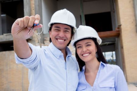 Couple at a construction site holding keys to their new house