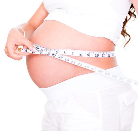 Pregnant woman measuring her growing belly - isolated over white