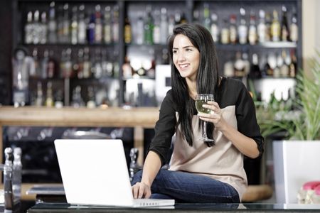 Beautiful young woman chatting with friends on her laptop while enjoying a glass of wine in a bar