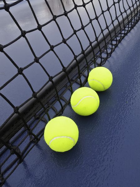 Three tennis balls by net on wet court after rain