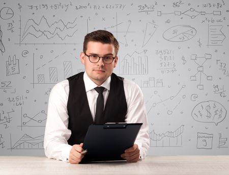 Young handsome businessman sitting at a desk with white charts behind him