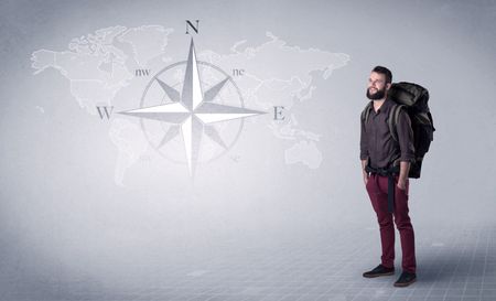 Handsome young man standing with a backpack on his back and a compass and a world map in the background
