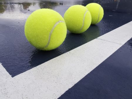 Three tennis balls in corner of a wet court after rain