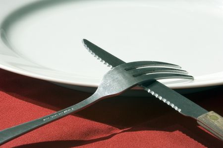 Fork crossed over serrated knife on white dinner plate