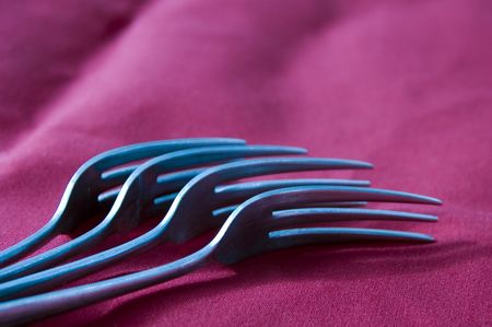 Four stainless steel forks on red linen napkin