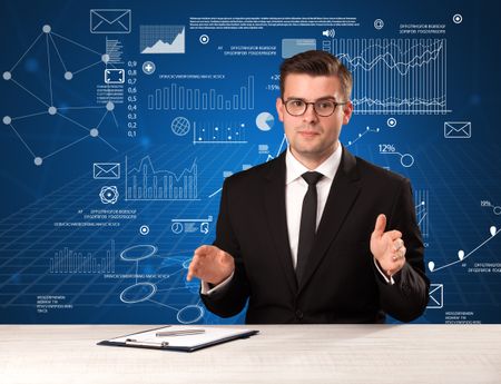 Young handsome businessman sitting at a desk with blue charts and data behind him