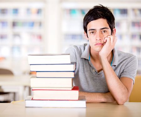 Bored male student at the library with a lot of books