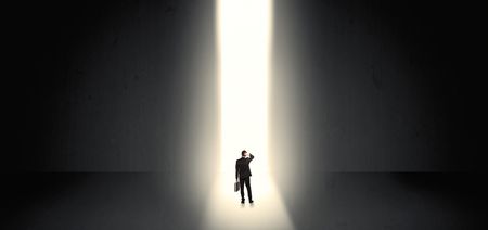 Businessman standing and seeing the light at the end of a big wall